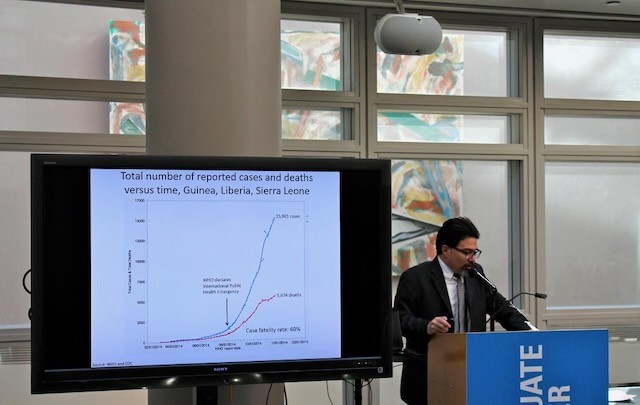 Denis Nash at a podium beside a chart of Ebola cases and deaths in Guinea, Liberia and Sierra Leone